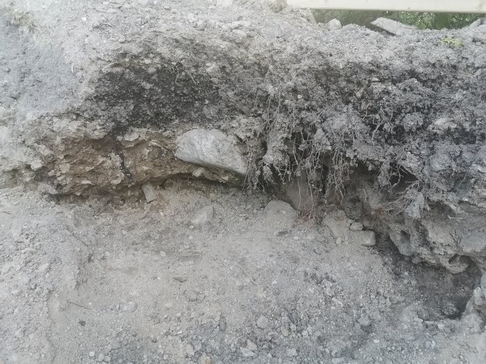 Sektion av grävt område med sten och sandiga kanter för anläggning av trädgårdsdamm.