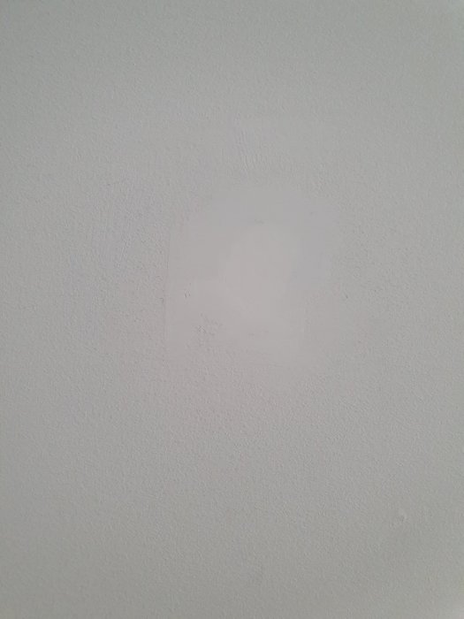 Vit vägg med ett större, ojämnt spacklat område som skiljer sig i färg mot resten av väggen.