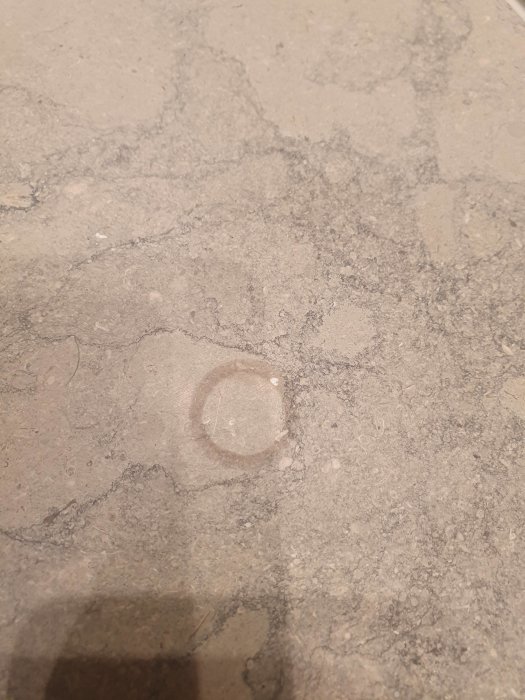 Rund fläck på grå stenskiva i badrum, omringad av suddiga konturer och mindre märken.