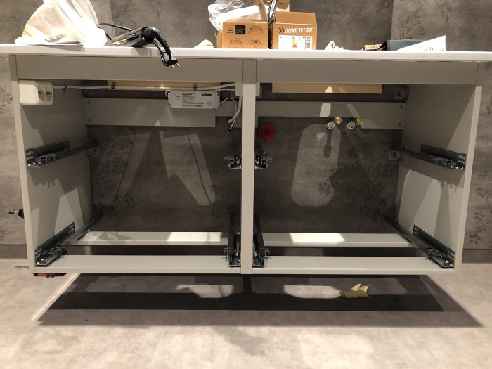 Ikea Godmorgon-kommod utan ben med synliga skenor och infästningar mot en tapetserad vägg under montering.