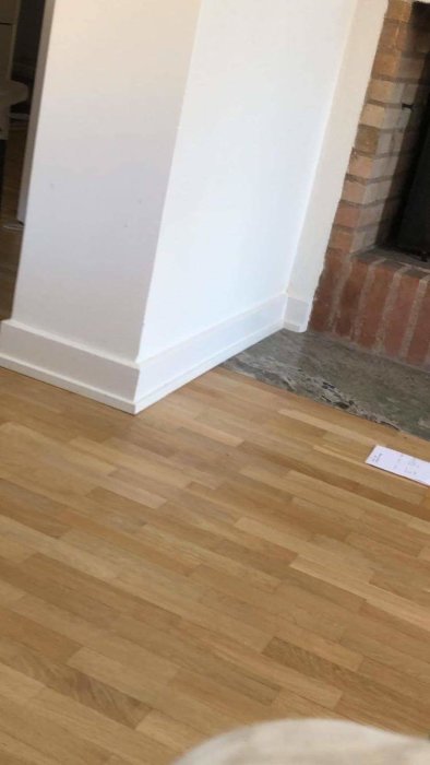 Enkel låg golvlist möter tegelsten vid en öppen spis, med parkettgolv i förgrunden.