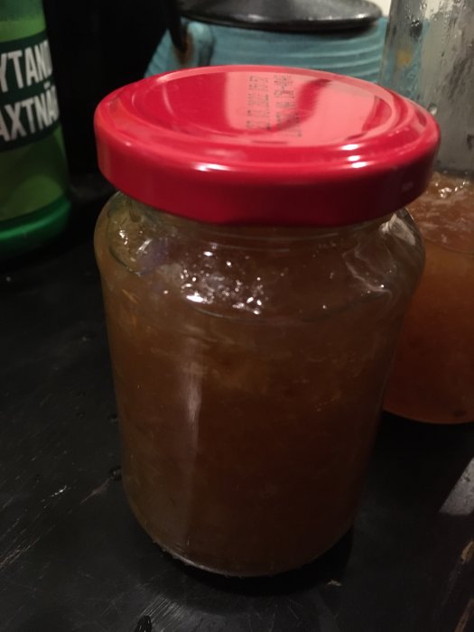 Burk med hemgjord fläder och citronmarmelad med rött lock på ett köksbord.