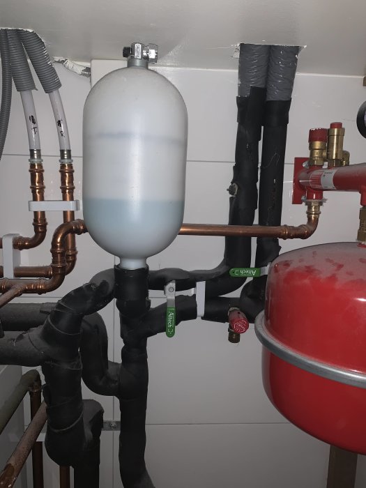 Bergvärmepumpsinstallation med två gröna ventiler och isolerade rör, expansionskärl och röda ventiler i ett värmesystem.