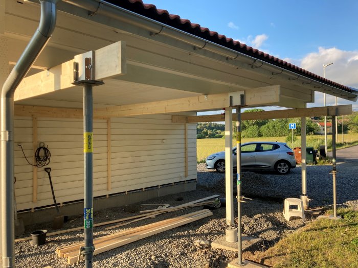 Byggprojekt med tre uppsatta balkar som förbinder en carport med en vägg, med tillfälliga pelare.