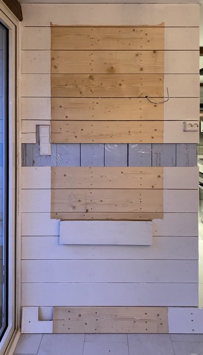 Ojämn vägg med glest monterade, breda träplankor och synlig byggplast bakom.