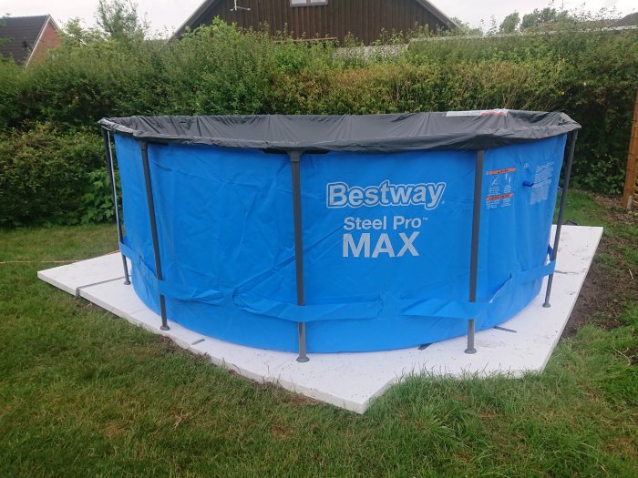 Bestway Steel Pro MAX ovanmarkspool monterad på vit plattform i en trädgård med grönt gräs.