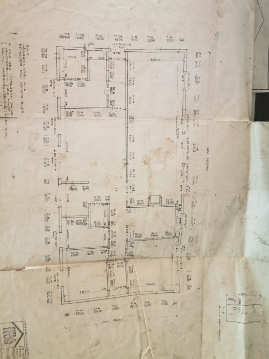 Gammal arkitektritning med mått och planlösning för ett hus, visar tecken på slitage och veck.