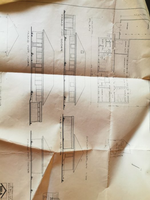 Ritade arkitektoniska plan- och fasadteckningar för ett husprojekt på ett vikt och något skrynkligt papper.