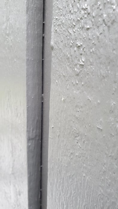 Glipa mellan nymålade stående och bakre paneler på husvägg, där färgen inte täcker.