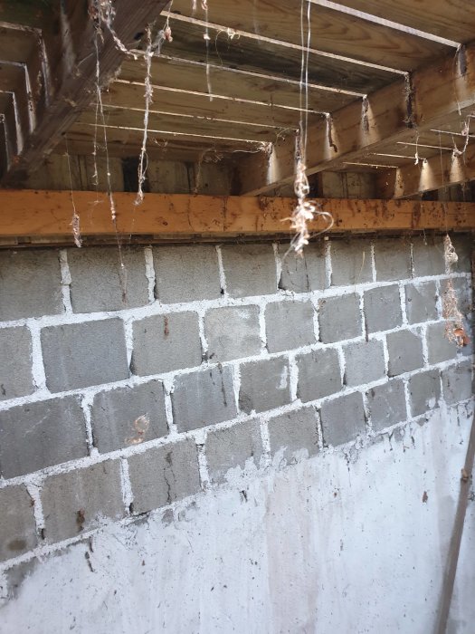 Utrymme under brokvist upptäckt vid renovering, synliga träbjälkar och grå murblock med spindelnät.