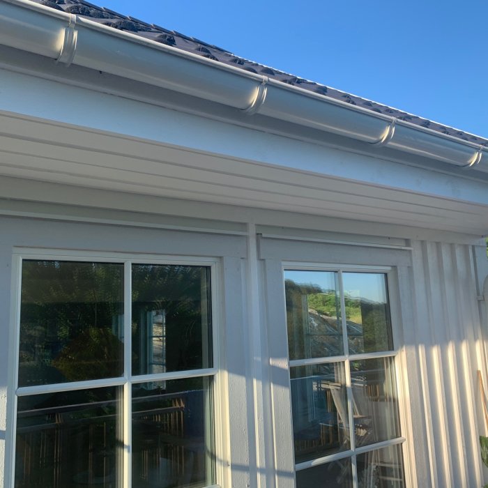 Vitmålat husutsprång och tak med fönster, möjlig fästpunkt för pergola.