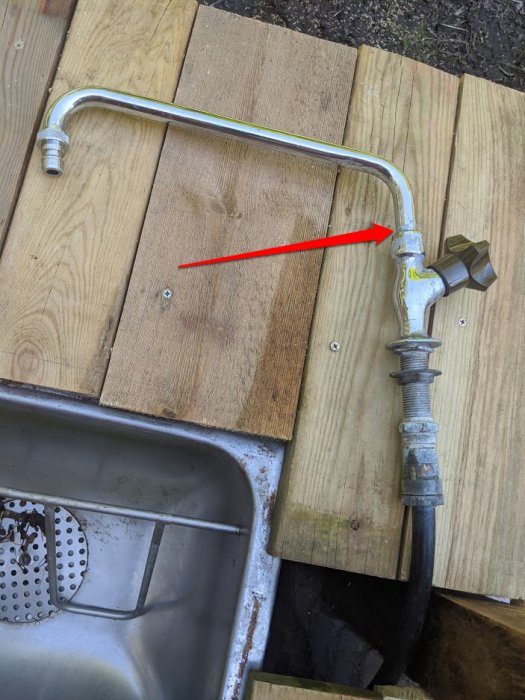 Gammal vattenutkastare monterad på träplankor markerad med röd pil där armen möter väggen, indikerande läckstället.