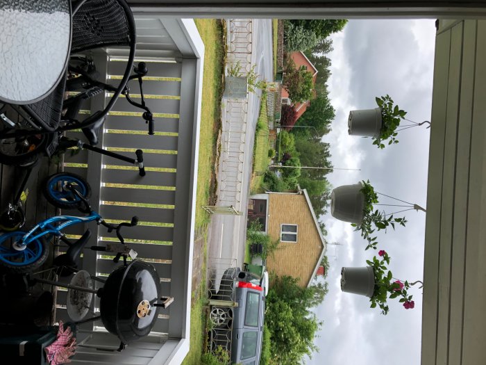 Vy från en balkong med en grill och cykel till vänster och upphängda växter till höger mot öppet uterum och bebodd byggnad i bakgrunden.