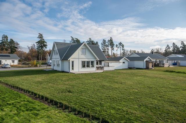 Vitt nybyggt hus med en grön gräsmatta och några häckar vid tomtgränsen under en klar himmel.