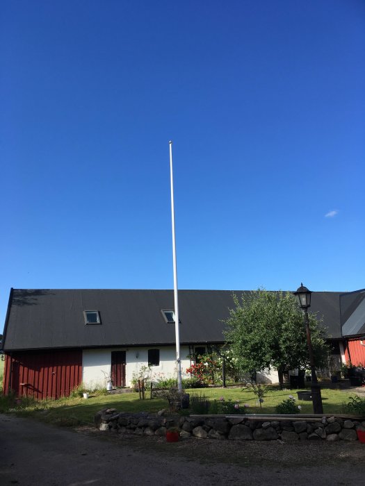 Röd och vit lantgård med en flaggstång framför under en klarblå himmel.