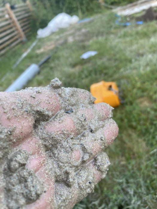 Närbild på en hand täckt med sand, suddig bakgrund av en trädgård.