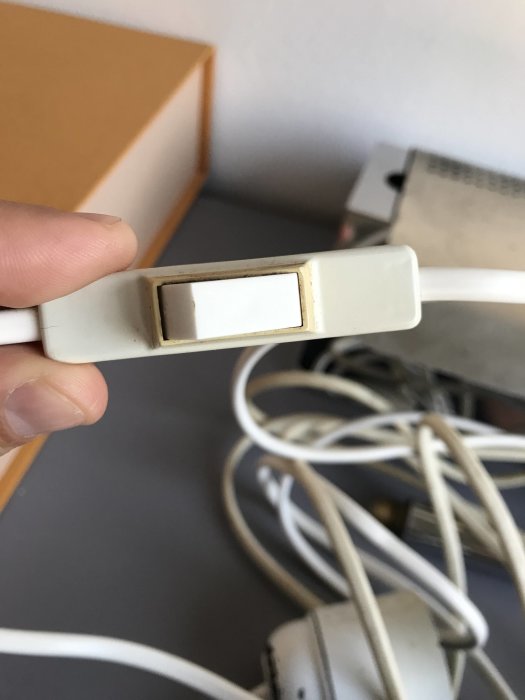 Vit strömbrytare på en sladd som hålls av en hand, vågig kabel och en del av en lampsockel syns suddigt i bakgrunden.