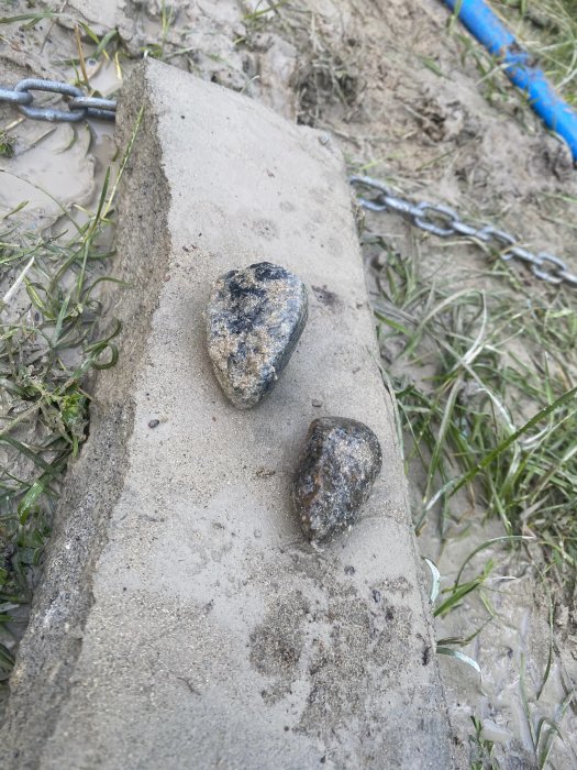 Två stenar på en betongkant med sand och gräs i bakgrunden.