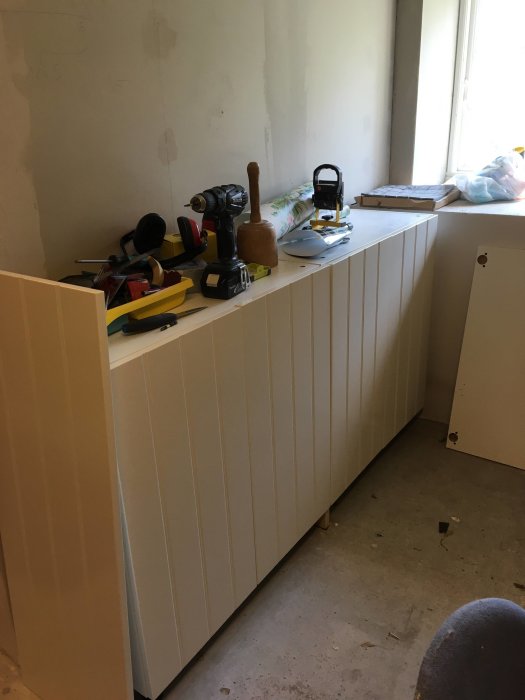 Köksskåp av olika höjd under renovering med verktyg och byggmaterial på bänk utan skiva.