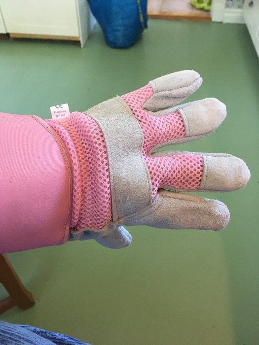 En hand iklädd en rosa arbets handske framför en grön bakgrund.