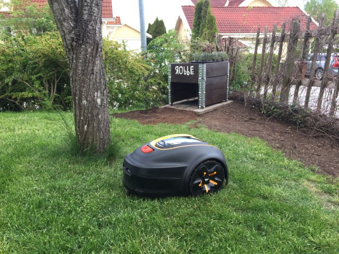 Robotgräsklippare "Robbe" på en gräsmatta med ett garage märkt på ett barnsligt sätt.