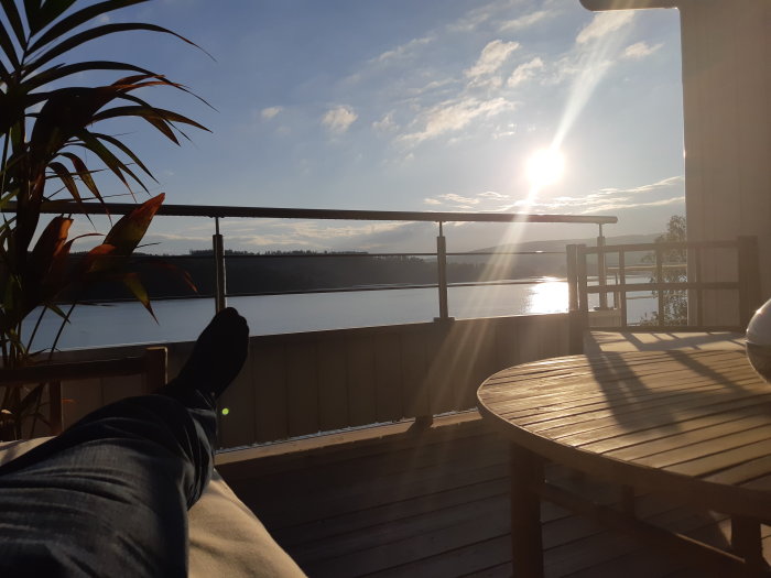 Person som avkopplar på en träaltan med utsikt över en sjö och skog vid solnedgång.