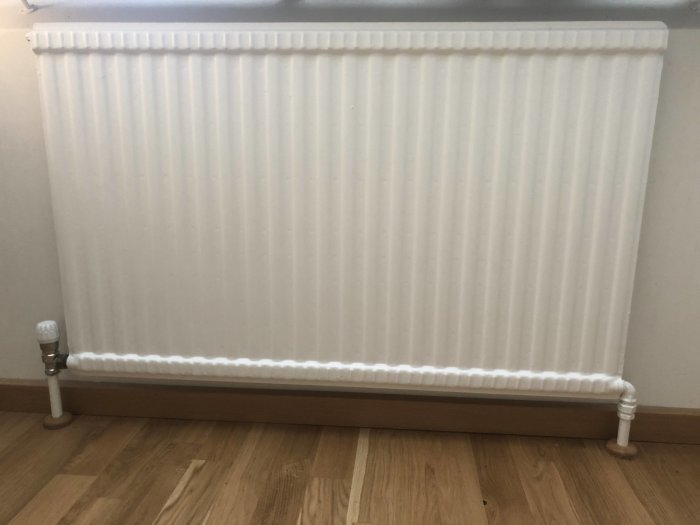 Enkelpanelradiator med inlopp och utlopp på ovanlig placering installerad vid vägg.