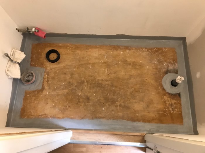 Golv under renovering med manschetter kring avlopp och tätad remsa längs mötet mellan vägg och golv.