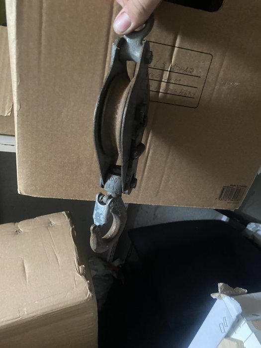 Hand som använder ett block och talja för att lyfta en tung kartong i en arbetsmiljö.