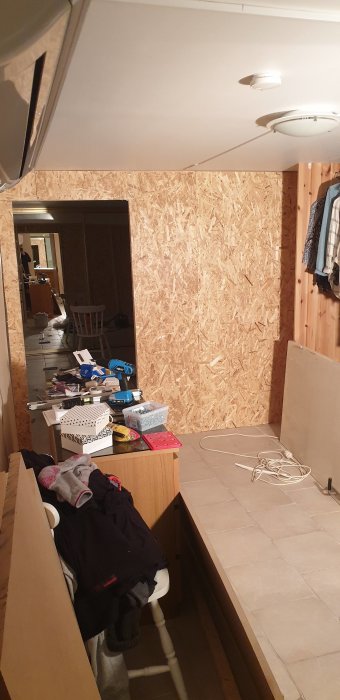 Halvfärdig walk in closet under konstruktion med OSB-skivor, byggmaterial och kläder.