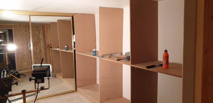 Pågående bygge av walk-in closet med icke helt raka MDF-skivor, verktyg och konstruktionsmaterial.