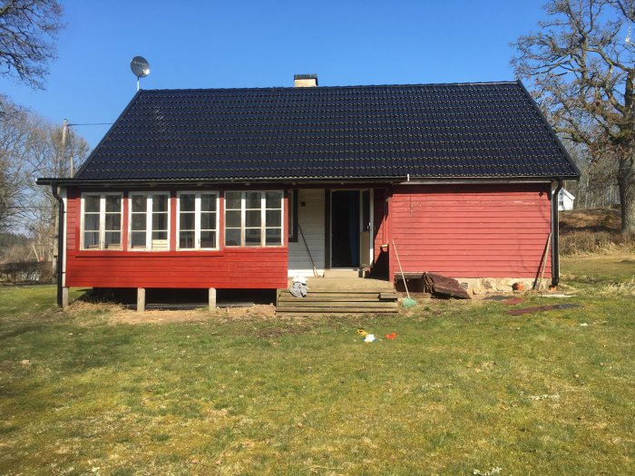 Hus med rött och vitt fasad, delvis nedmonterat trädäck och matkällaringång, innan renovering.