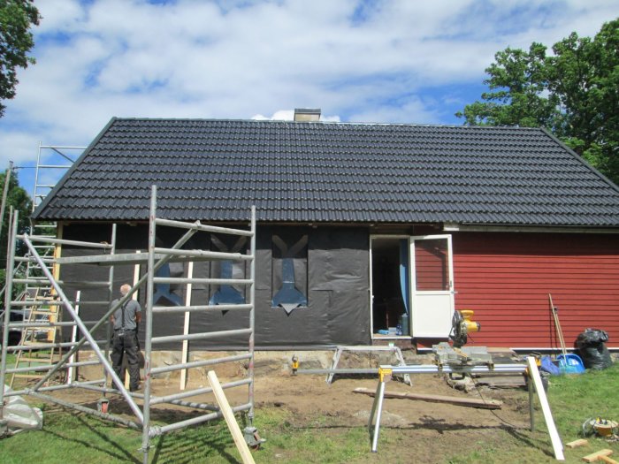 Pågående byggnadsarbete av trädäck vid en röd husfasad med byggställningar och öppen altandörr.