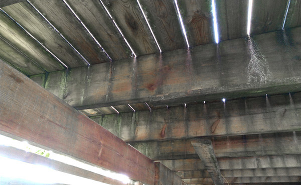 Undersidan av en altan med bärlinor och golvreglar synliga, potentiellt i behov av förstärkning.
