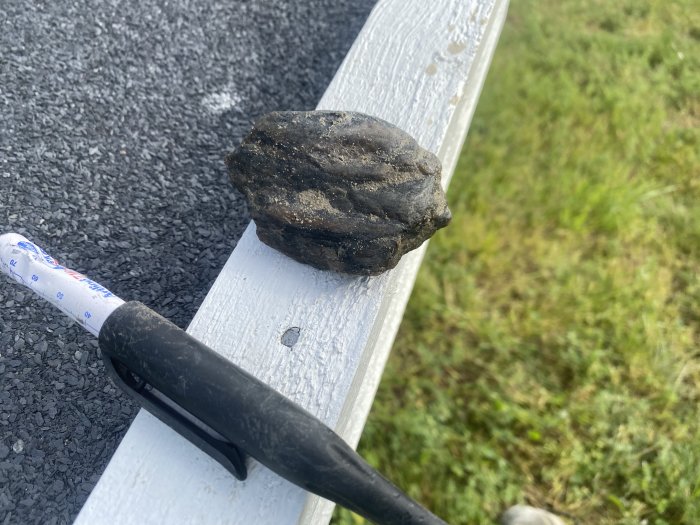 En stor sten som ligger på en vit markering vid en asfalterad väg med en hammare bredvid.