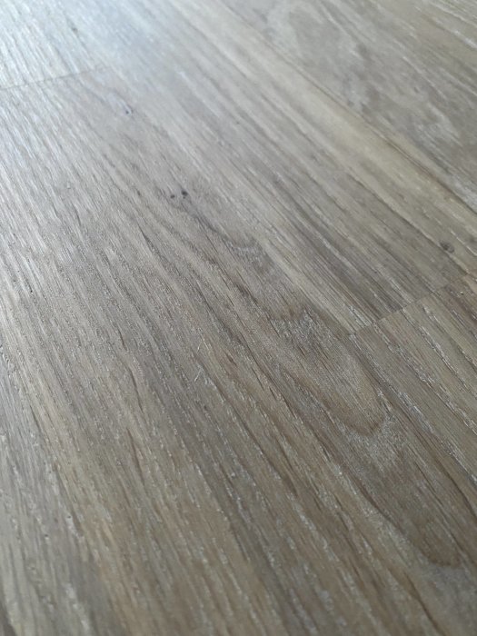 Närbild av ett nyligen slipat ekgolv med fläckar och sträva fibrer som sticker upp.