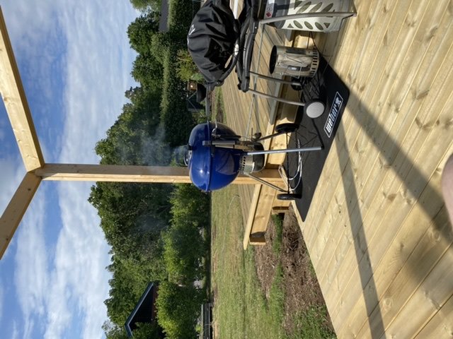 Nybyggd trall med en grill och utemöbler, omgiven av grönska.