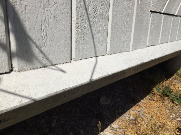 Närbild på grund av en solbänk mot en vitmålad vägg, visar konstruktion med träplugg och skuggspel.