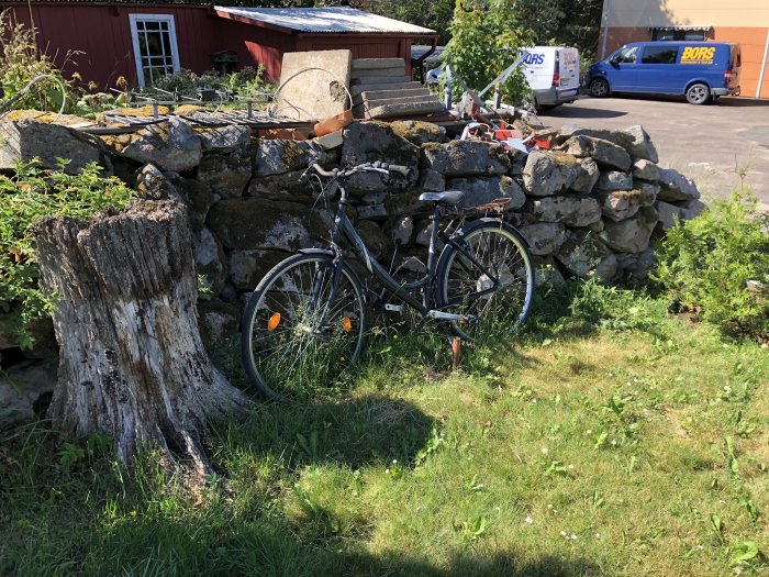 Gamla stenmuren på en tomt med synlig skada, cykel parkerad framför och bakgrund med grönska.