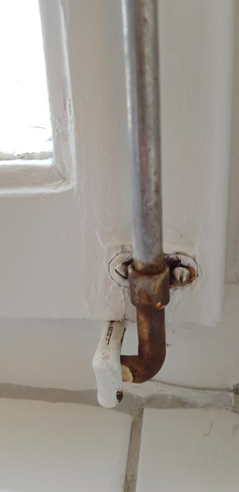 Rost på metallskena och fönsterlås i badrum, med tecken på korrosion och skador på ytan.
