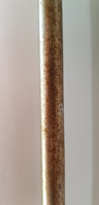 Närbild på ett rostigt metallrör, troligen en del av ett badrumsfönster.