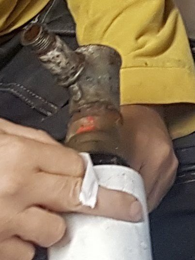 Rostig gammal tryckströmbrytare som tas bort från vit 1/2-tums rörledning med hand som håller torkpapper.