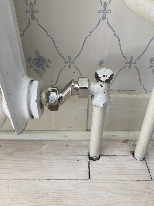 Radiator med kopplingsdetalj vid golv intill tapetserad vägg, förslag på installation för sänkning av element.