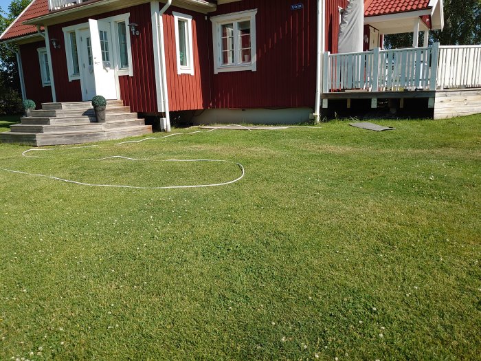 Kabel dragen över gräsmattan med hus och trädäck i bakgrunden på en solig dag.