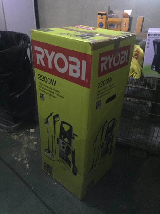 En ny Ryobi högtryckstvätt i sin förpackning står på en balkong, redo att användas när vädret svalnar.