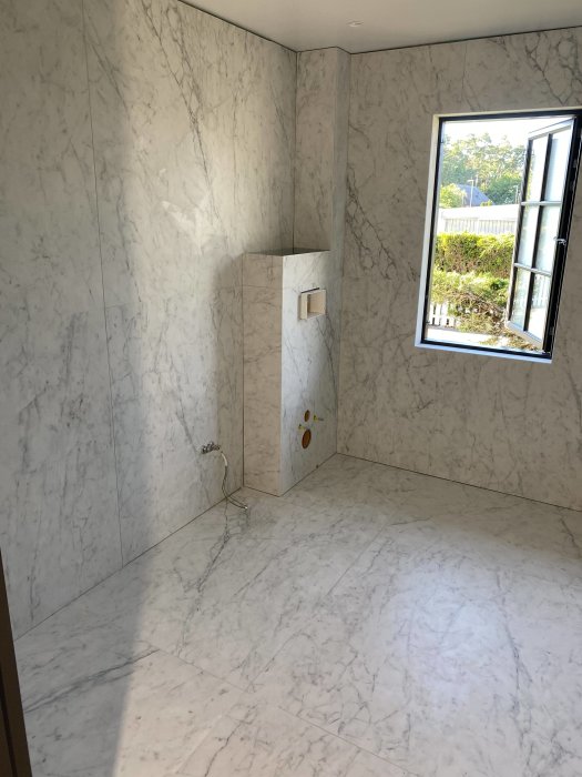 Badrum med marmormönstrade plattor i formatet 120x120 cm på både väggar och golv, inklusive en nisch och golvvärme installation.