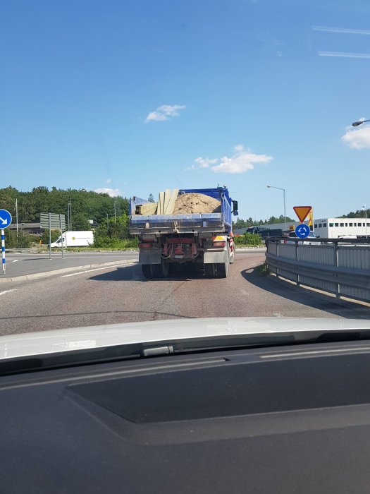 Lastbil med överhängande byggmaterial kör försiktigt i en rondell.