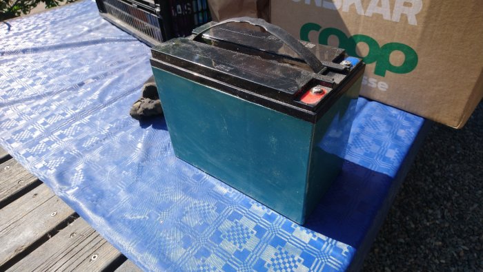Ett tungt batteri på en blå presenning med en kartong från Coop i bakgrunden.