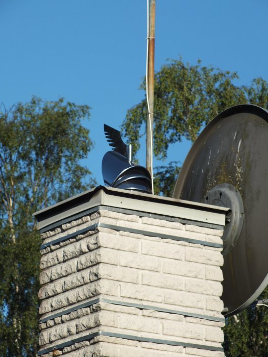 Skorstensskydd på en tegelskorsten som reflekterar solen mot grannens hus.