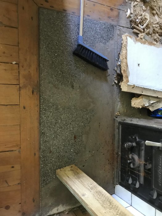 Grovstädning av ett renoveringsprojekt nära en spis med synlig grå sten och en sopborste.